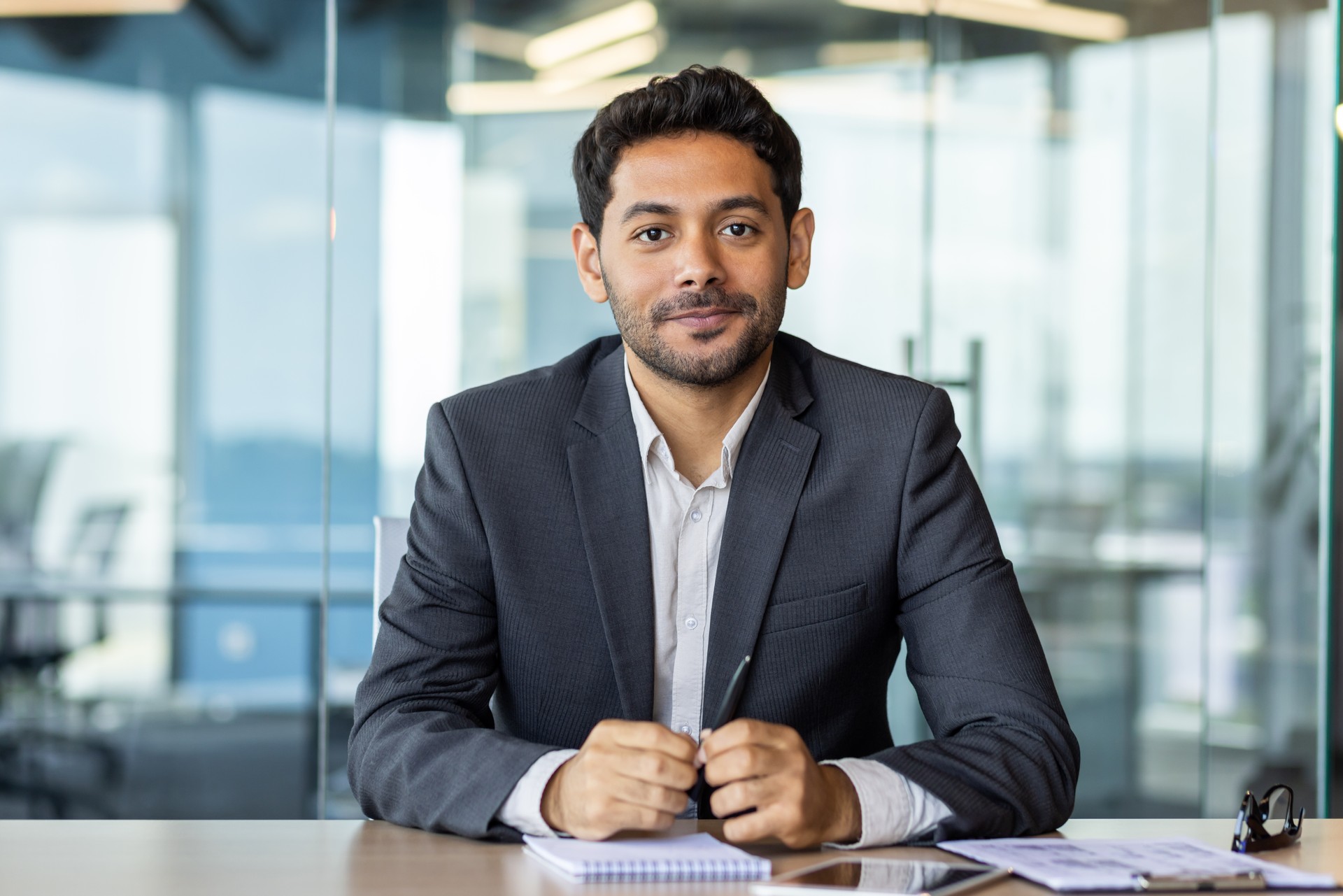 Portrait of a young investor banker at the workplace inside the bank office, a businessman in a business suit looking friendly at the camera, a man at work Portrait of a young investor banker at the workplace inside the bank office, a businessman in a business suit looking friendly at the camera, a man at work